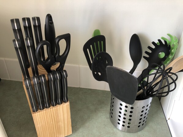 A kitchen utensil holder with various utensils, a metal colander, and a wooden spoon. - Gorgeous view 2 Storey Townhouse 2 BR/1.5 Bath, A/C, Hot Tub, Fire Pit (Harvie Heights)