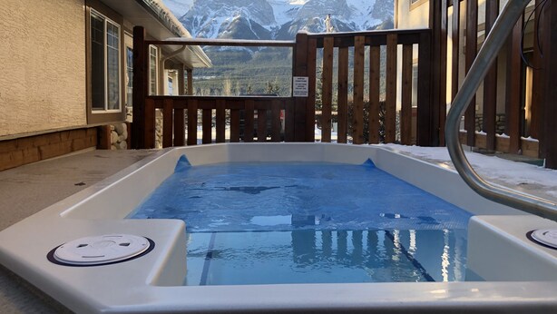 A hot tub with a wooden deck and a view of snow-covered mountains. - Gorgeous view 2 Storey Townhouse 2 BR/1.5 Bath, A/C, Hot Tub, Fire Pit  (Harvie Heights)