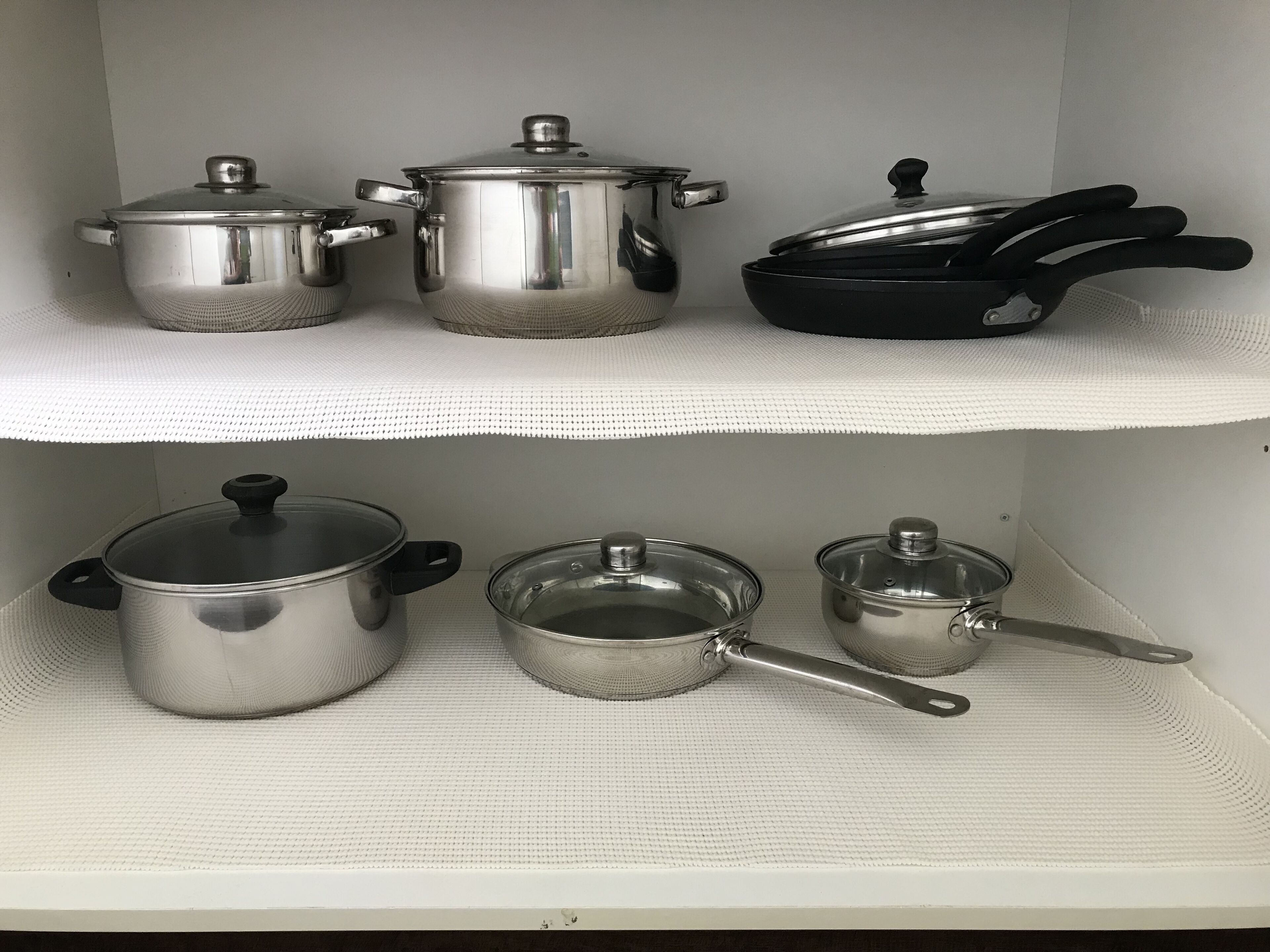 A kitchen shelf with various cookware items including pots, pans, and a frying pan.