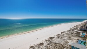 Une plage avec une eau d’un bleu limpide, un rivage sablonneux et des bâtiments dotés de piscines.