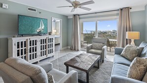 A living room with a TV, sofa, armchairs, a coffee table, and a balcony with a view. - Emerald Coast Vibes & Sunset Views – Islander 517 (Destin)