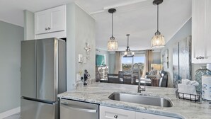 A modern kitchen with a stainless steel refrigerator, a marble countertop, and pendant lighting. - Emerald Coast Vibes & Sunset Views – Islander 517 (Destin)