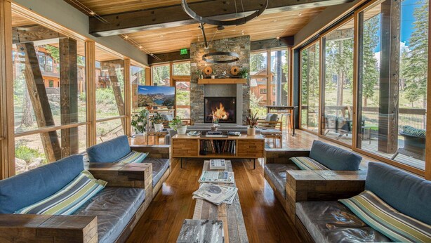A spacious room with a fireplace, wooden furniture, and large windows offering a view of the outdoors. - Gondola Ski-in/Ski-out By Tahoe Getaways - Luxury 4 BR, Private Hot Tub, Access to Pool (Truckee)