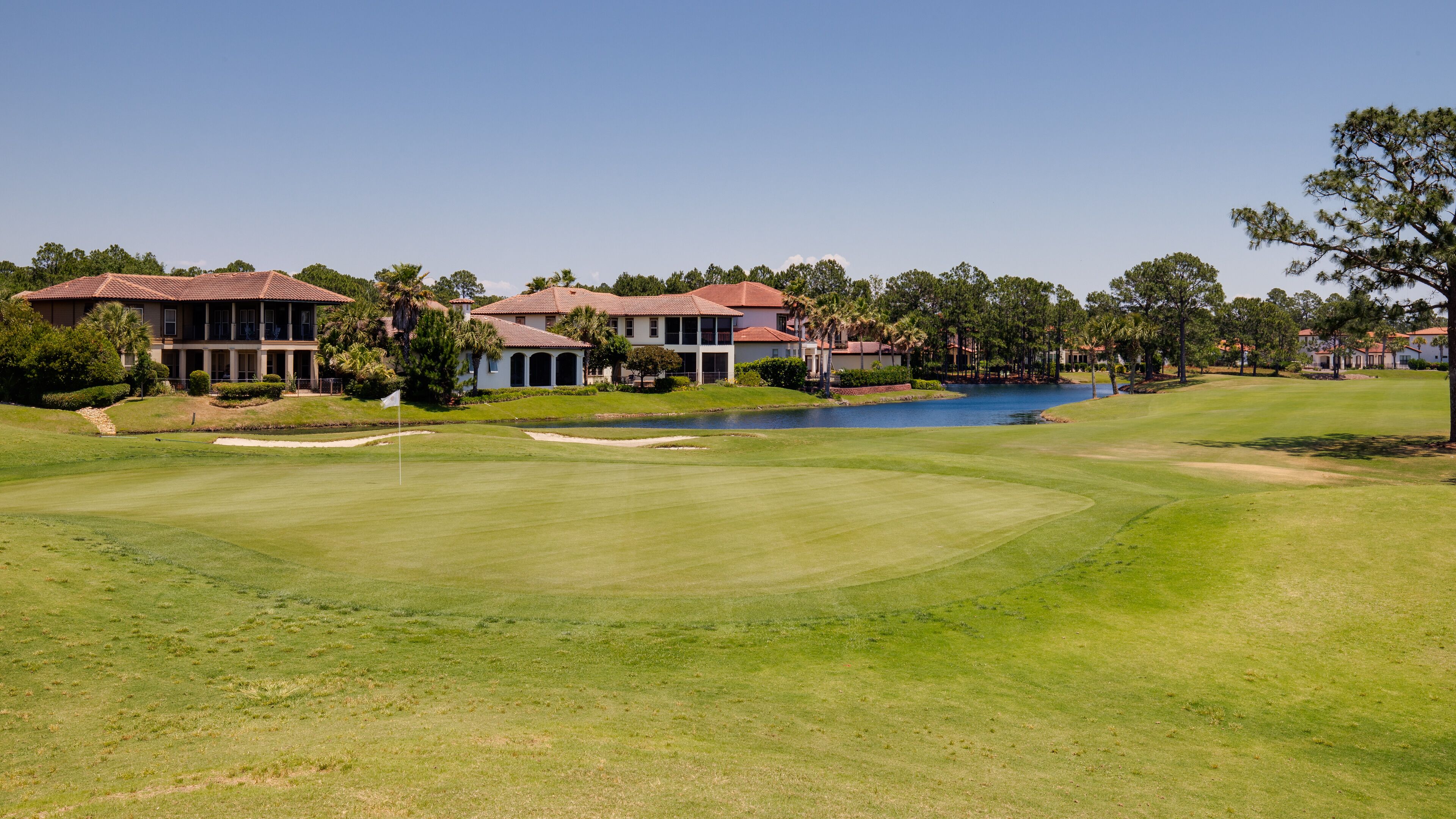 A golf course with a pond, surrounded by residential buildings with red-tiled roofs.