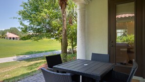 An outdoor patio with a table and chairs, a view of a lawn and a building in the background. - 4BR Beach Villa w/ 2 GOLF CARTS! Near Pool & Wharf. Beach Tram. Covered Patio (Miramar Beach)