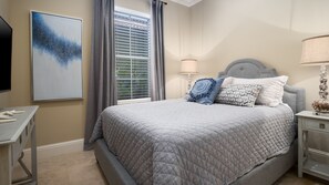 A bedroom with a bed, a nightstand, a lamp, a painting, and a window with curtains. - 4BR Beach Villa w/ 2 GOLF CARTS! Near Pool & Wharf. Beach Tram. Covered Patio (Miramar Beach)