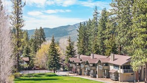 A row of single-story buildings with a flat roof, surrounded by dense coniferous trees and a mountain in the background.