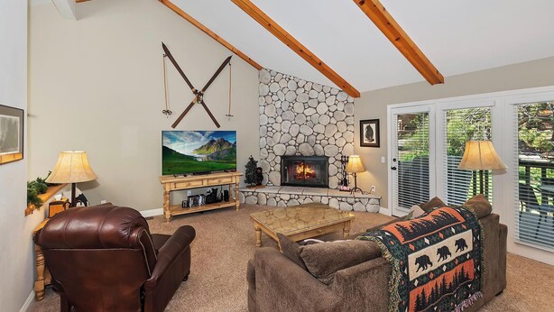 A cozy living room with a stone fireplace, wooden beams, a television, and a comfortable sofa.
