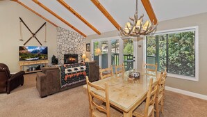 A cozy living room with a stone fireplace, a television, and a dining area with a glass-top table and wooden chairs.