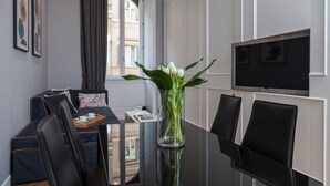 Una habitación de hotel moderna con zona de comedor, un ventanal grande y un televisor de pantalla plana montado en la pared.