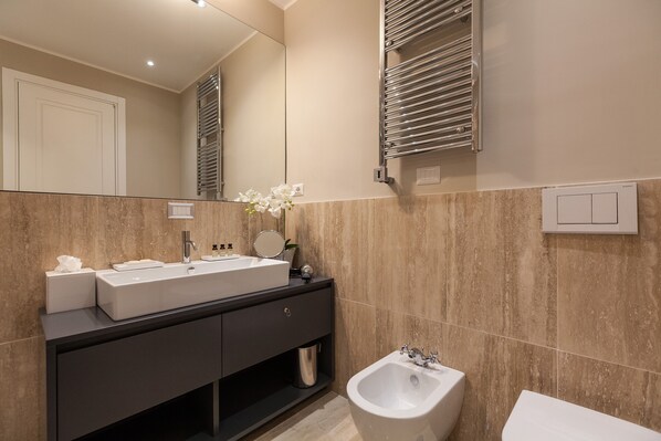 Une salle de bain moderne avec un grand miroir, un lavabo blanc, un bidet et un meuble-lavabo foncé.