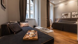 Una habitación de hotel moderna con una cama, una mesita de noche con una bandeja de tazas de té, un sofá y vistas a un edificio a través de una ventana.