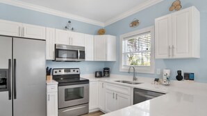 A modern kitchen with white cabinets, stainless steel appliances, and a window with blinds.