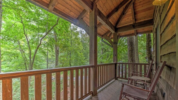 A wooden porch with a railing, rocking chairs, and a view of a forest.