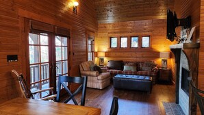A cozy cabin interior with a wooden interior, a fireplace, a dining area, and a seating area with a couch and chairs.