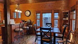 A wooden cabin interior with a dining area, bar, and large windows.