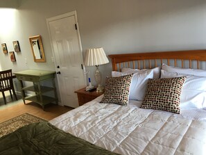 Ein Schlafzimmer mit einem Bett, Kissen, einem Schreibtisch, einem Stuhl und einer Tür.