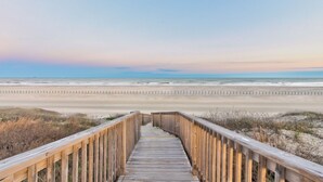 Un paseo marítimo de madera que lleva a una playa bajo un cielo despejado.