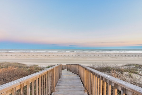 A wooden boardwalk leading to a beach with a clear sky.