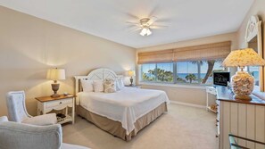 A bedroom with a bed, bedside tables, a chair, a desk with a lamp, a ceiling fan, and a window with blinds. - 442 Captains Walk - Palmetto Dunes - Updated Direct Oceanfront Villa - Sleeps 6! (Hilton Head Island)