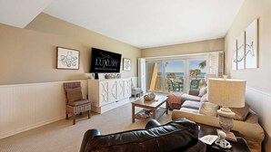 A spacious living room with a large TV, comfortable seating, a dining area, and a view of the ocean. - 442 Captains Walk | Direct Oceanfront Views (Hilton Head Island)