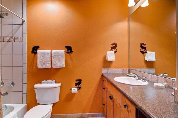 Et badeværelse med orange væg, et hvidt toilet, en vask og et bruseområde.