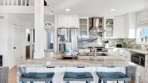 A modern kitchen with white cabinets, a marble countertop, and a stainless steel refrigerator.