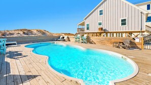 A wooden deck with a swimming pool, lounge chairs, and a large building with a balcony.