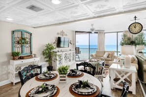 Enjoy a view of the sea from the living room and dining area, featuring a large wall-mounted clock and a television.