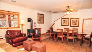 A living room with a leather sofa, a dining table with chairs, a fireplace, and a ceiling fan. - River Tranquility managed by Cabin Butler (Greer)