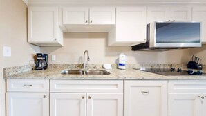 Una cocina con armarios blancos, un fregadero de acero inoxidable, una cafetera y un microondas.