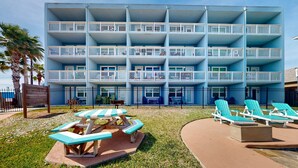 Un hotel de varios pisos con balcones, un área de piscina con sillones de descanso y una mesa de picnic.