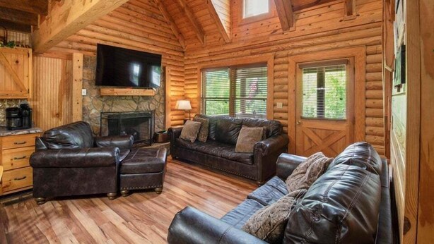 L’intérieur d’une cabane en rondins, avec une cheminée, des canapés en cuir et un téléviseur à écran plat.