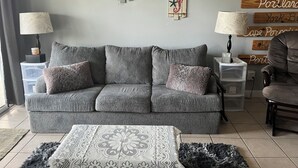 A living room with a grey sofa, two side tables with lamps, a patterned rug, and wooden wall decorations. - Waterfront Condo Within Steps To Wells Beach!  (Wells)