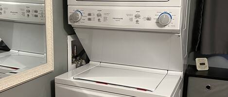 A compact laundry room with a front-loading washer and dryer, a wooden table, and a mirror.