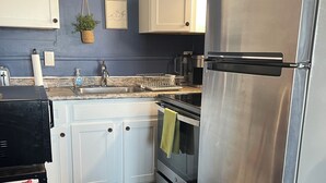 A compact kitchen with white cabinets, a stainless steel refrigerator, a built-in oven, and a sink. - Waterfront Condo Within Steps To Wells Beach!  (Wells)