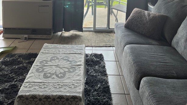 A living room with a sofa, a patterned ottoman, a ceiling fan, and a sliding glass door leading to an outdoor area with a table and chairs. - Waterfront Condo Within Steps To Wells Beach!  (Wells)