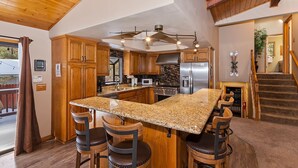 Una cocina moderna con armarios de madera, una isla de granito y electrodomésticos de acero inoxidable.