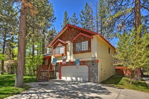 A two-story house with a stone foundation and a red roof, surrounded by tall pine trees.