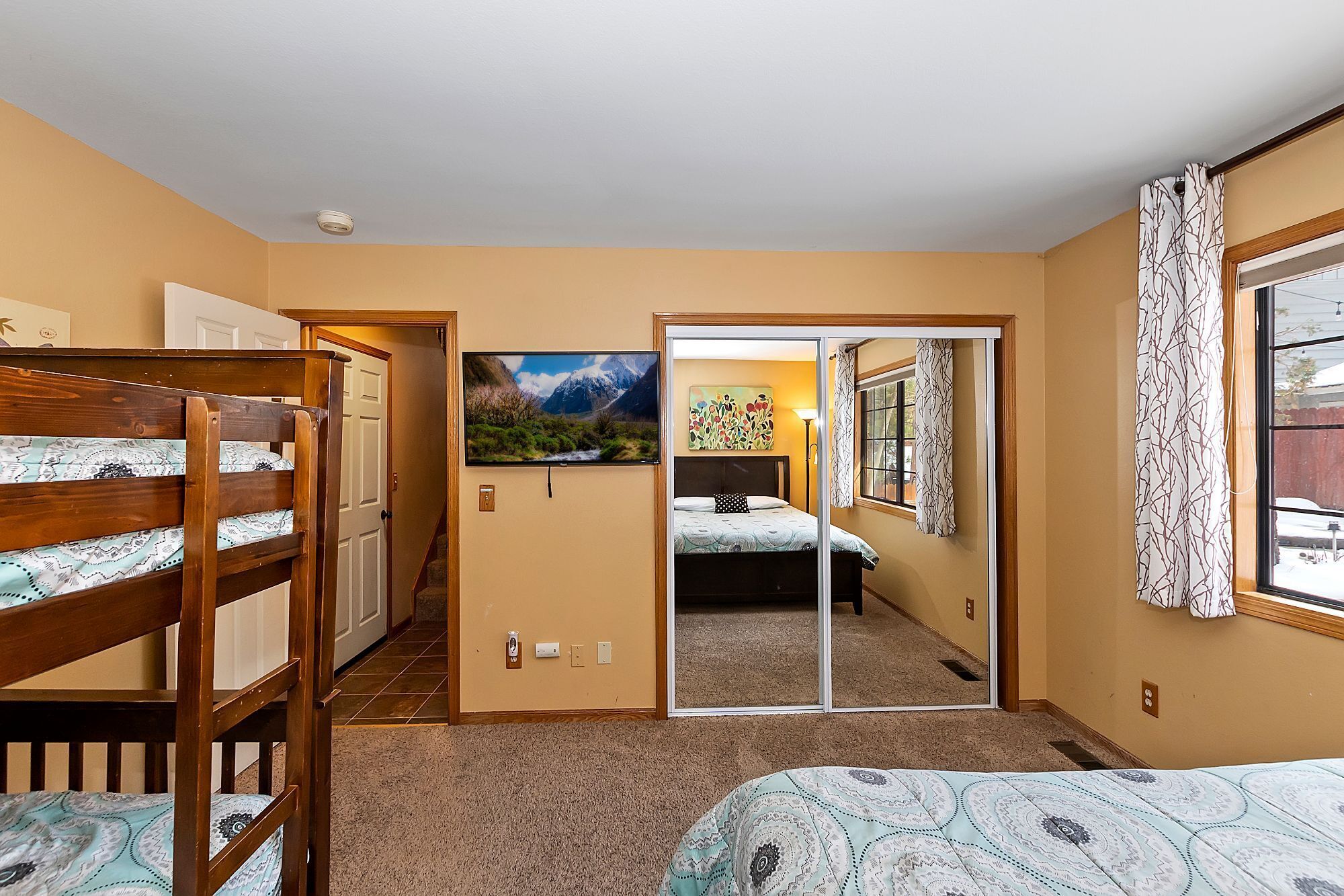 Un dormitorio con literas, un ventanal con cortinas estampadas, un cuadro y una puerta corredera que da a otra habitación.