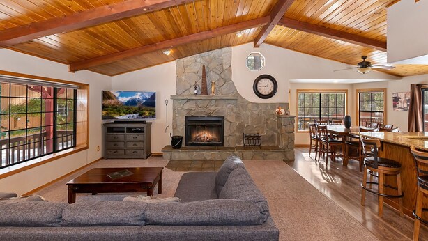 Un amplio salón con chimenea de piedra, un sofá grande, una televisión y un comedor con barra.