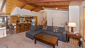 Amplia sala de estar con un sofá seccional gris grande, una mesa de centro de madera y una cocina al fondo.
