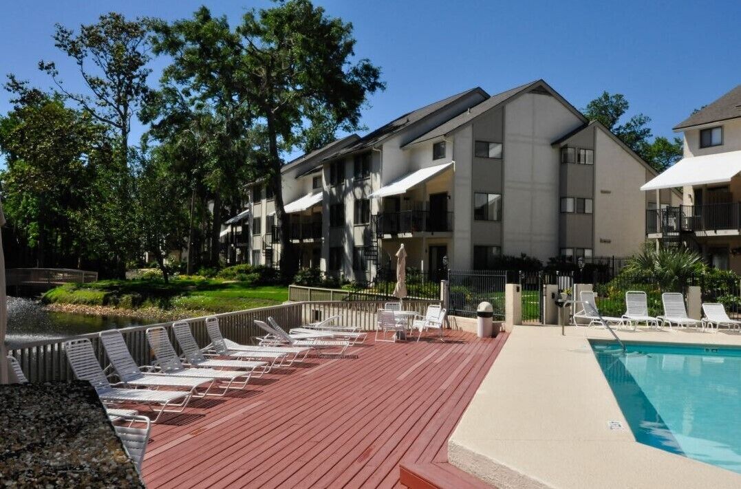 A poolside area with lounge chairs, a pool, and a building with balconies.