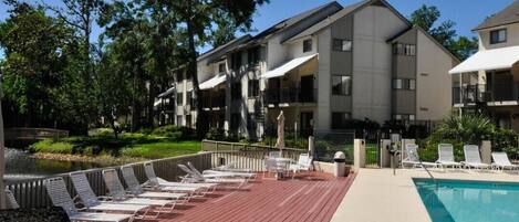 A poolside area with lounge chairs, a pool, and a building with balconies.