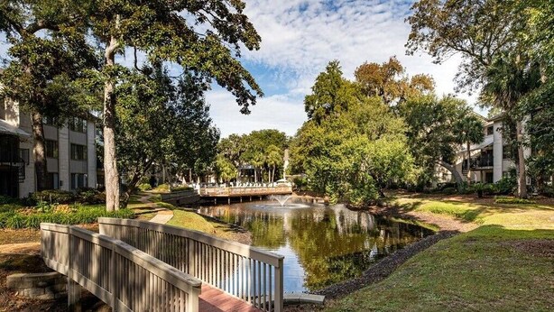 A serene courtyard with a pond, a wooden bridge, and lush greenery.
