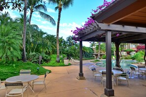 A covered outdoor area with a pool, lounge chairs, and palm trees. - Beautiful Ocean Views From Maui Kamaole I-118   (Kihei)