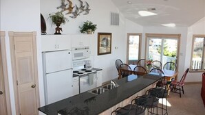 A modern kitchen with a central island, white cabinetry, and a dining area with chairs and a table. - Let yourself be "Swept Away"  BOOK OUR BEAUTIFUL HOME NOW FOR 2026 (Corolla)