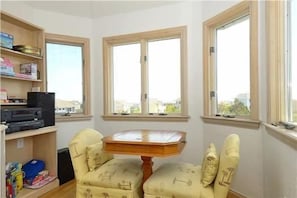 A room with a wooden table and two chairs, a bookshelf, and three windows.