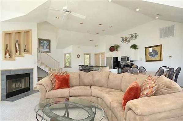 A spacious living room with a curved sofa, a glass coffee table, and a fireplace.