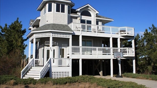 A two-story house with a balcony, a staircase, and a basketball hoop. - Let yourself be "Swept Away"  BOOK OUR BEAUTIFUL HOME NOW FOR 2026 (Corolla)
